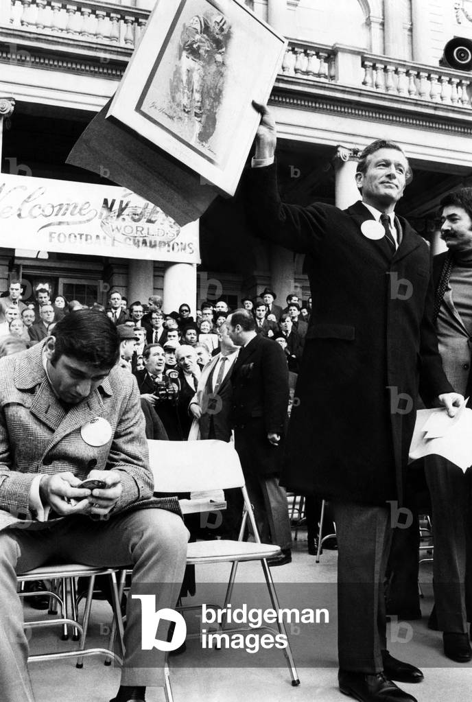 Joe Namath, examines a bronze medallion presented to him by New York City Mayor John Lindsay. Mayor Lindsay holds a picture of Namath in action. Six thousand fans cheered Namath and booed Lindsay at the celebration, January 22, 1969