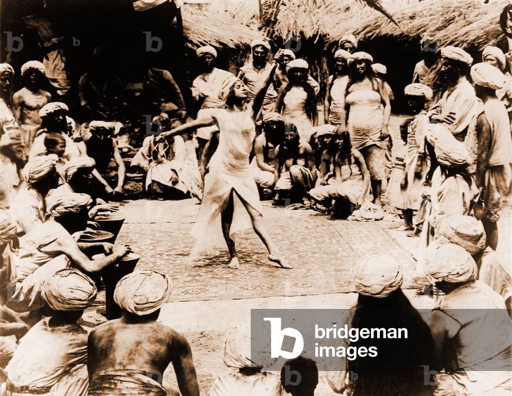 Nautch girl, a young Indian dancing on rug with Hindu men and women watching. India, 1914