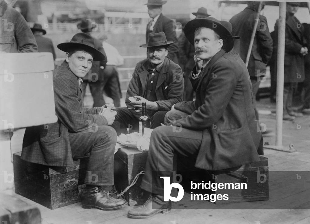Three cheerful men (probably Germans), share a meal and a bottle on the immigrant ship the PRESIDENT GRANT of the Hamburg American Line at the end of its voyage in New York Harbor. c. 1910