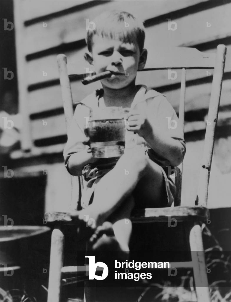 World's 'toughest' 3-year-old, sits in chair holding mug of beer while smoking a cigar, 1935