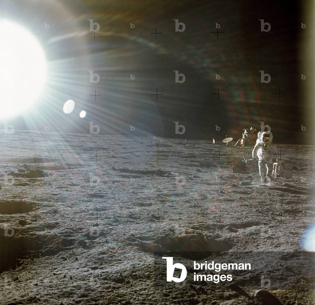 Apollo 12 Astronaut Alan Bean deploys scientific experiments on the lunar surface. The bright flare of light is caused by the Sun. The Lunar Lander is in the distance. Nov. 19, 1969
