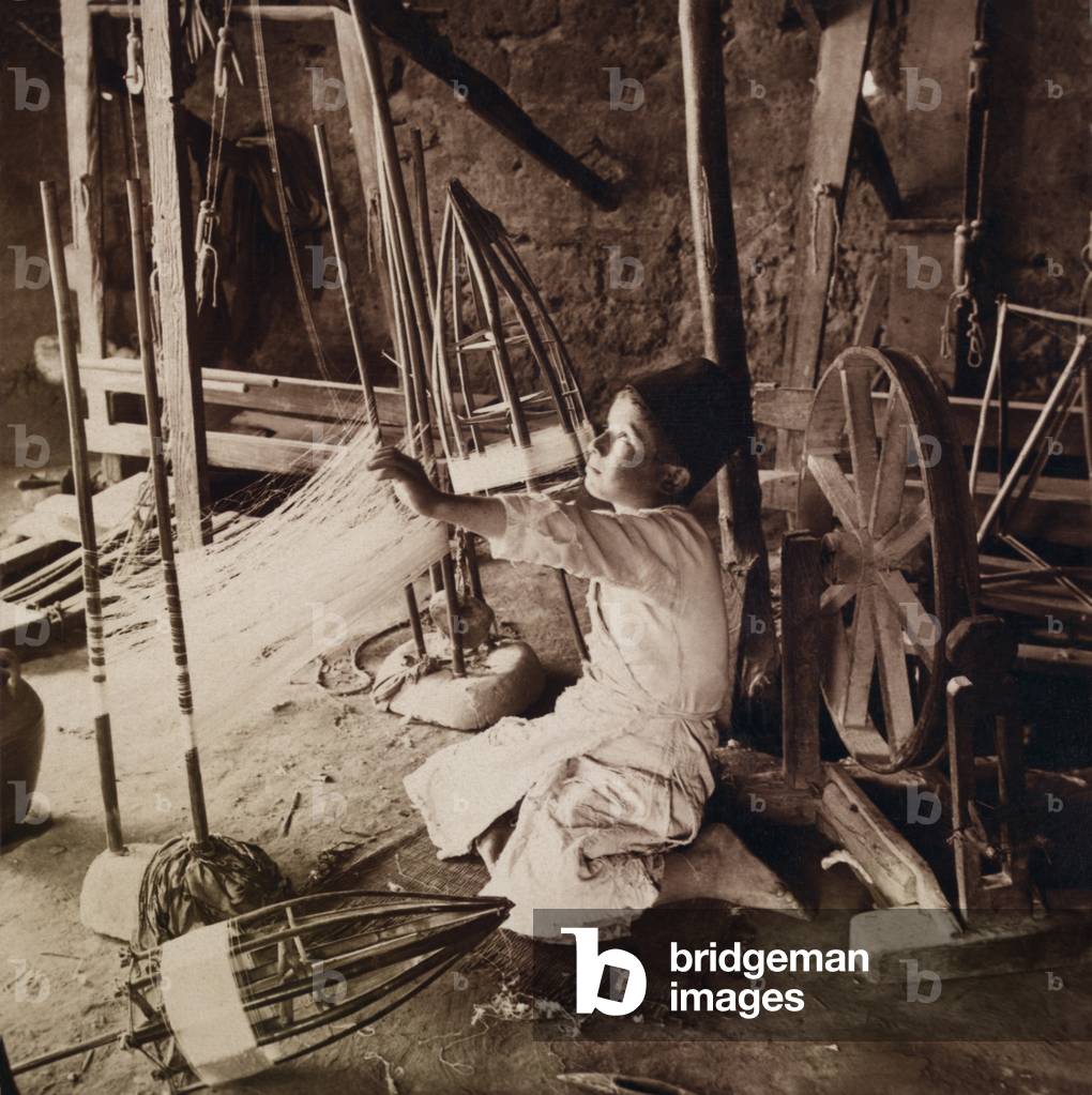 Young boy unwinding silk cocoons and reeling silk threads with pre-industrial tools in his Syrian home in 1914