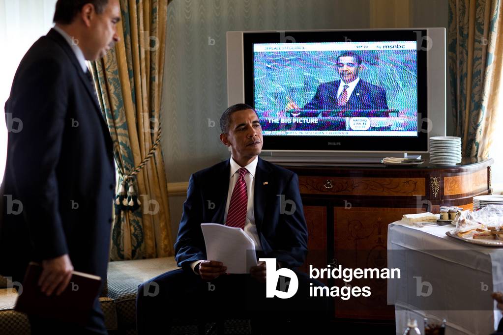 President Barack Obama in front of a television showing his UN speech while he is in his room at New York's Waldorf Astoria Hotel before his meeting with Russian President Dmitry Medvedev. On left is with Senior Advisor David Axelrod. Sept. 23 2009.,