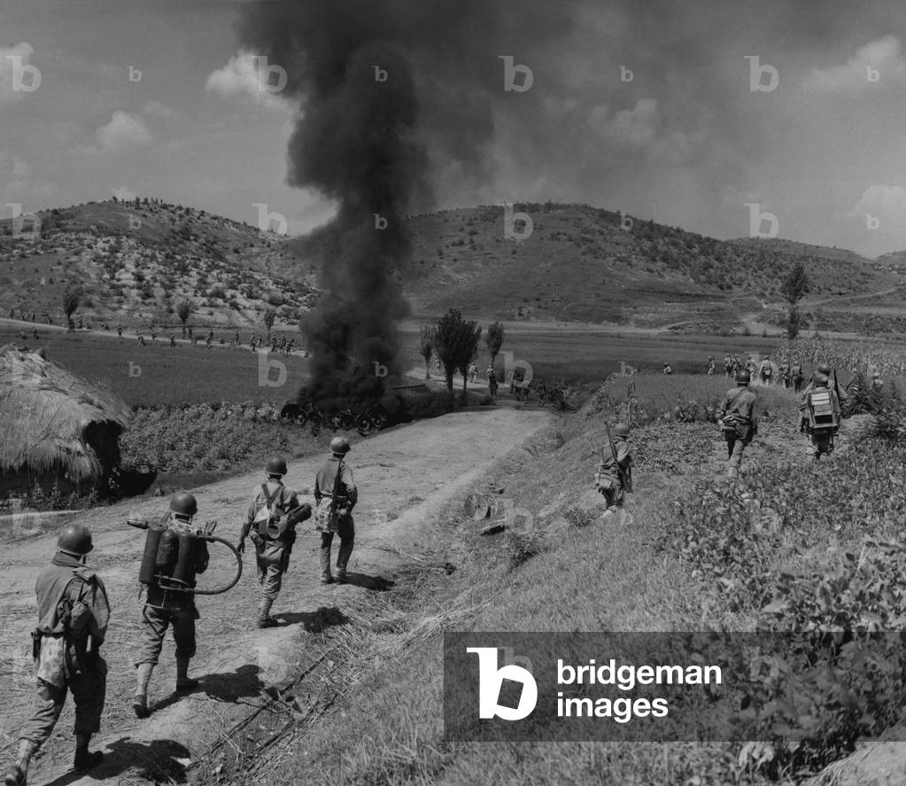 U.S. Marines advancing in the Naktong River Battle, Sept. 4, 1950. The men in the column are spaced out to avoid casualties and walk around the burning North Korean tank. Second from left Marine carries a flame thrower, and the man in front of him has a rocket launcher. Battle of Pusan Perimeter. Korean War, 1950-53