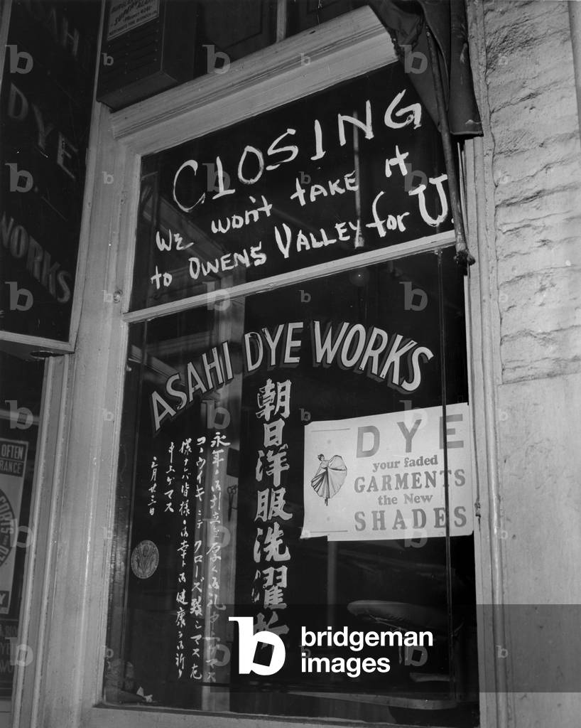 World War II, Shop window of Asahi Dye Works with sign reading: 'Closing, we won't take it to Owens Valley for U', just before the Japanese were evacuated from Little Tokyo to the War Relocation Center, in Owens Valley, a typed caption reads 'War Migration of Japanese', Los Angeles, California, April, 1942