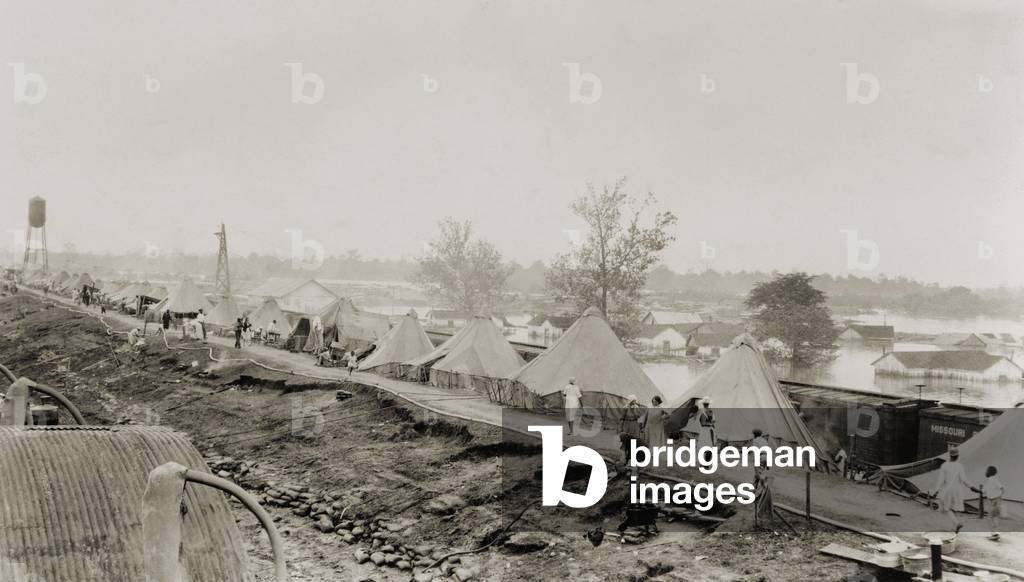 Refugees at a tent city on the levee, with partially submerged houses of Arkansas City in background, during the 1927 Flood