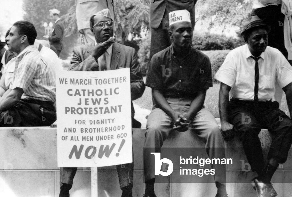 Civil Rights, the civil rights march from Selma to Montgomery, Alabama in 1965. Photograph shows some participants in the civil rights march sitting on a wall resting, one holds a placard which reads, 