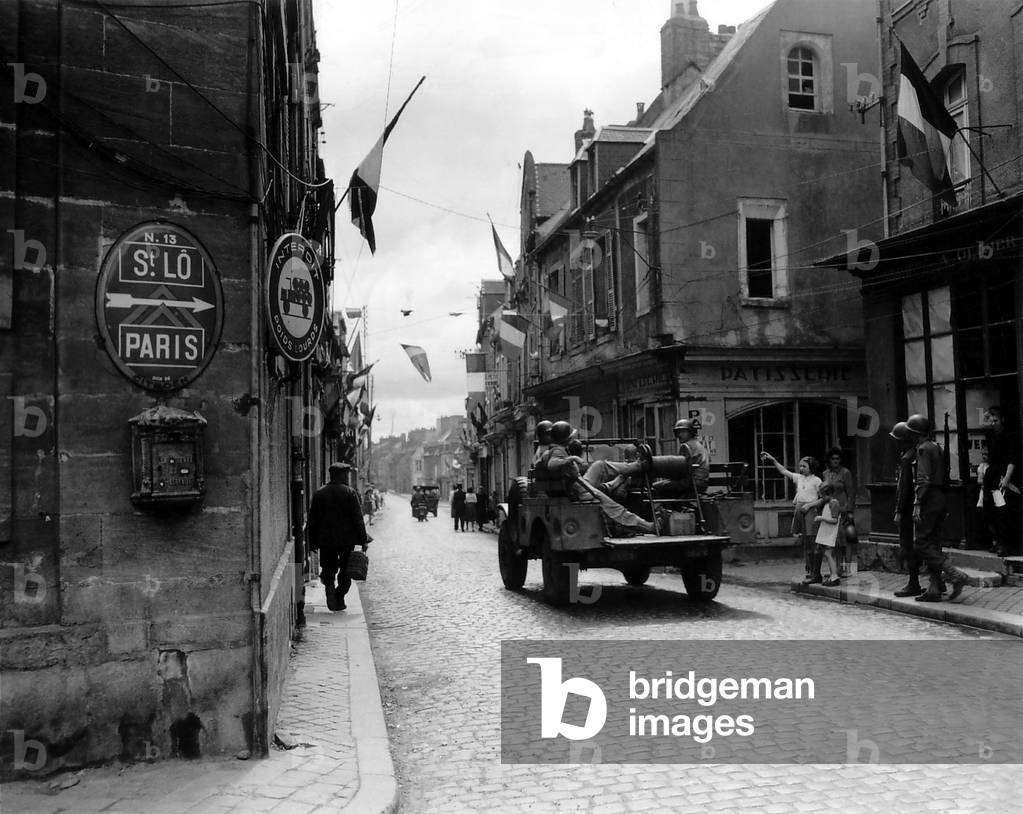Five U.S. soldier ride through Carentan, France, on the road to Saint-Lo, June 12, 1944. French flags decorate the street of the newly liberated town. Normandy Campaign, France, World War 2