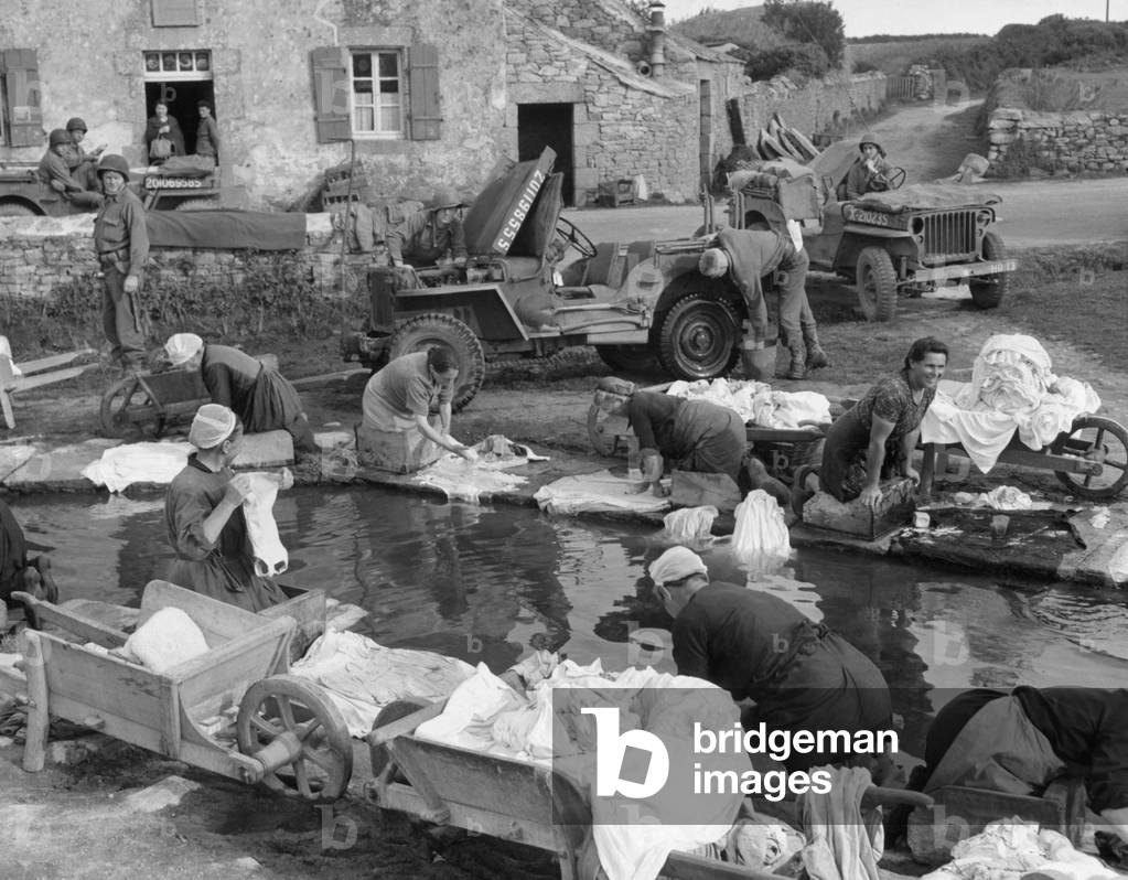 French village women doing their share their laundry facility with GI's washing their Jeep. Sept. 20, 1944, World War 2