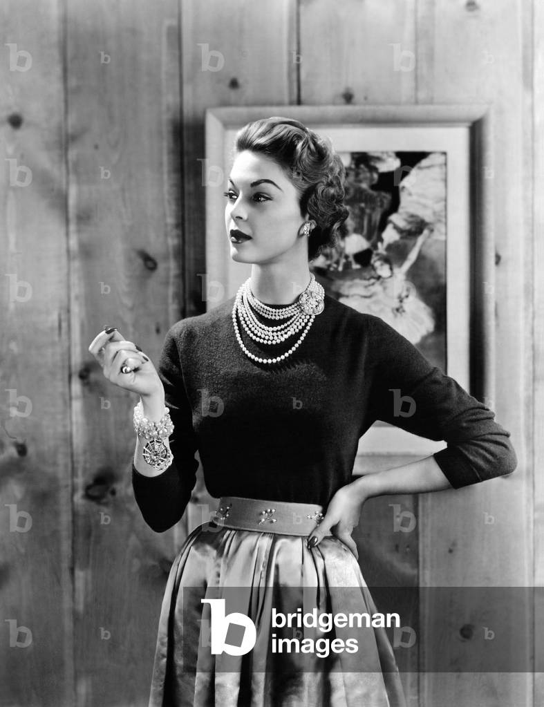 Black cashmere pullover is worn with a satin gathered full skirt and wide belt emphasizing the narrow waist. Dior's new look dominated women's wear for several years after it introduction in 1947. Oct. 1953