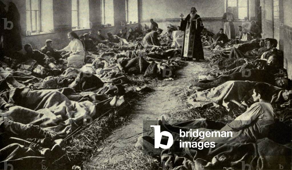 World War 1. Russian soldiers wounded at Dunajec. An old priest of the Greek Catholic Church comforting the wounded and dying Russians as they lie on the straw covered stone floor. May 1915