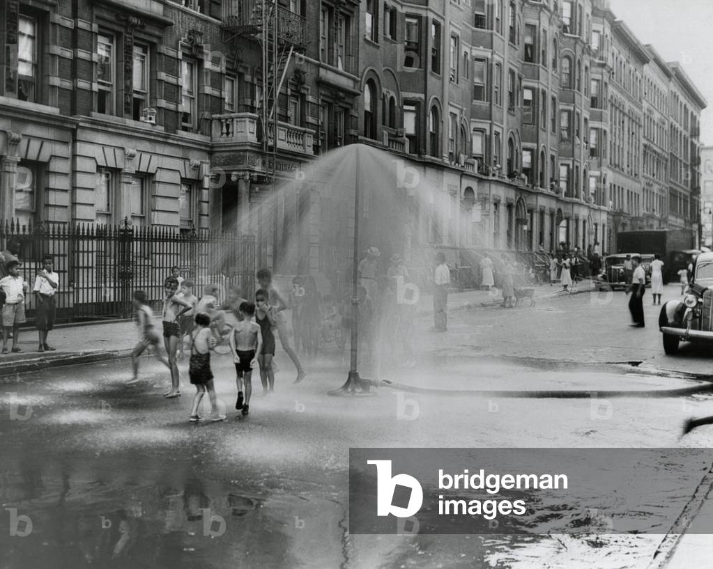 African American children playing in water sprayed from a sprinkler in South Harlem, NYC, Aug. 8, 1937