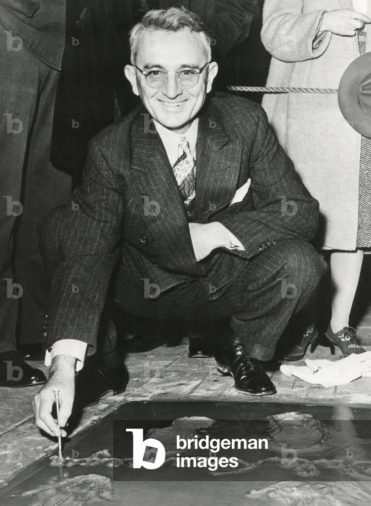 Dale Carnegie, signing his concrete slab at Grauman's Chinese Theatre. His book, 'How To Win Friends and Influence People' of 1931 is a classic and still relevant self-help book. c. 1930s.