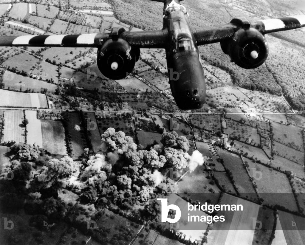 Aerial view of a A-20 G Havoc light bomber with D-Day 'invasion stripes' painted on its wings. Plumes of smoke rise from the Forest Cerisy, where a German Machine gun position blocked the U.S. advance. Allied domination of the air was critical to the success of the Normandy invasions. June 8, 1944. World War 2