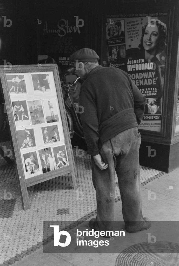 Elderly man with patches clothing looking at stills of Joe Lewis fight. Windsor Locks Connecticut. Oct. 1939