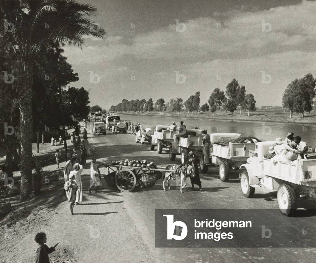 British Army moves to forward areas around El Alamein and El Darba. Egyptian villagers watching a large British convoy of military trucks traveling along the road to the Western Desert during World War 2. c. 1940-42