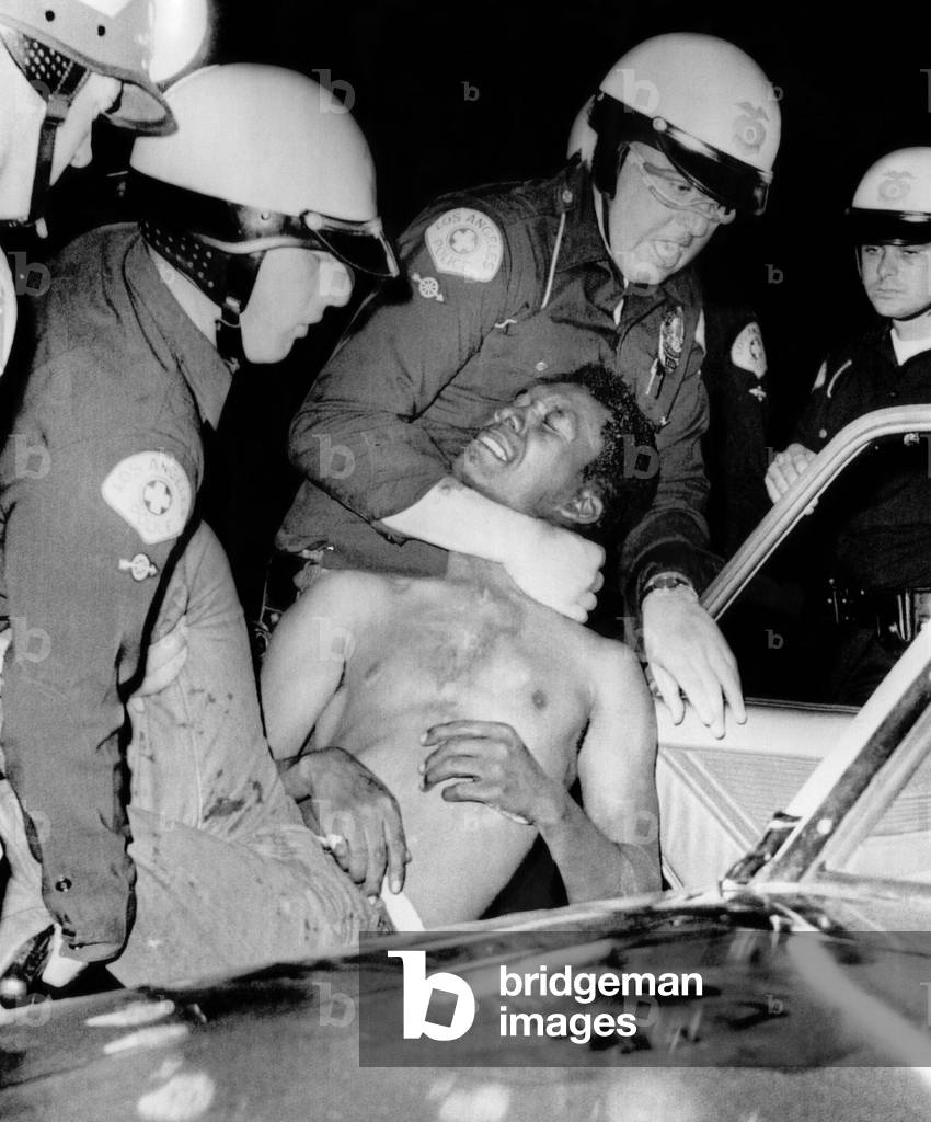 Policemen force a man into a police car during the riots in Watts, 1965