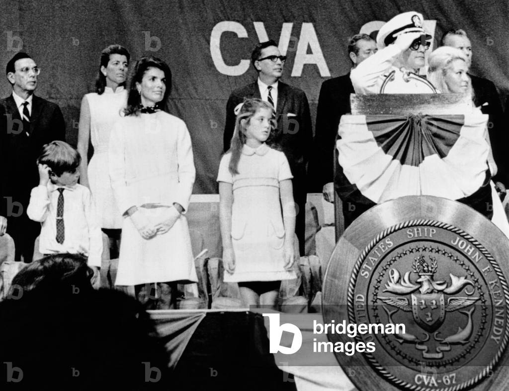 Captain Earl Yates (on right, saluting), the commanding officer of the new aircraft carrier USS John F. Kennedy during the commissioning ceremonies. Kennedy's widow Jacqueline and children, Caroline and John Jr. look on. Also Attending were Patricia Kennedy Lawford (back row) and Joan Kennedy (far right). August 7, 1968