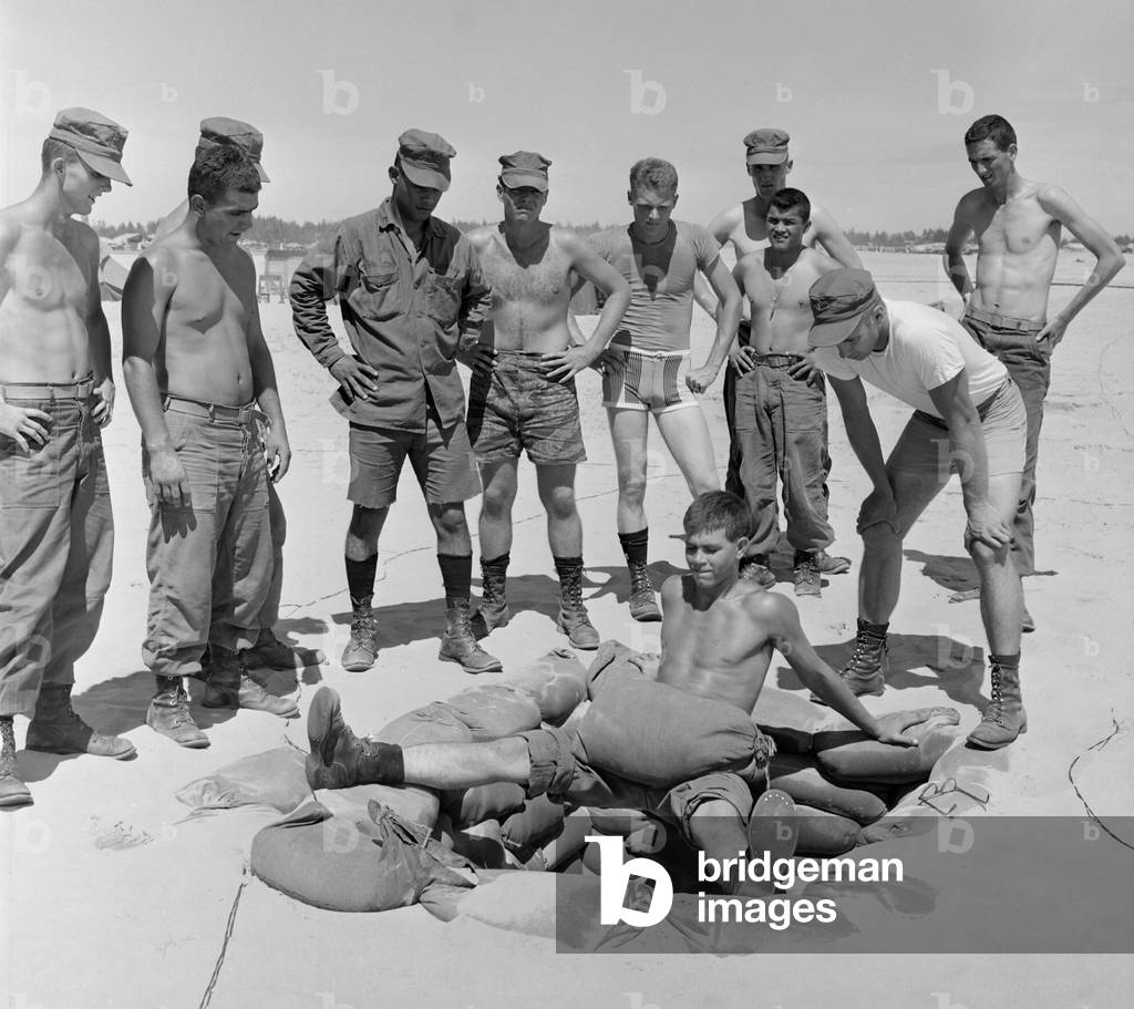 Vietnam War. US Marine Lieutenant instructs soldiers in an extreme leg and stomach muscle exercise performed over a sandbagged foxhole. Aug. 13, 1966
