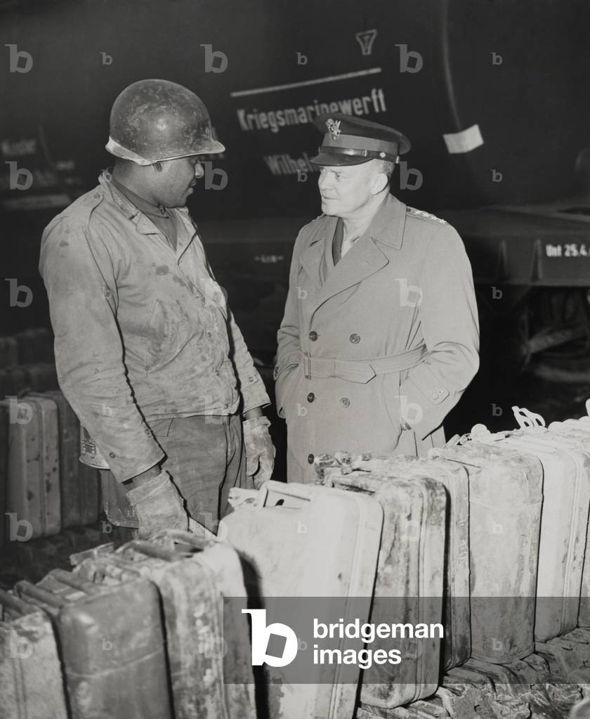 General Dwight Eisenhower talks with African American Private Edward Clay. Clay is stationed at a gas dump on the Western Front. The sign in background, 'Kriegsmarinewerft Wilhelmshaven', indicates the location is the coastal town in northwest Germany. c. 1945