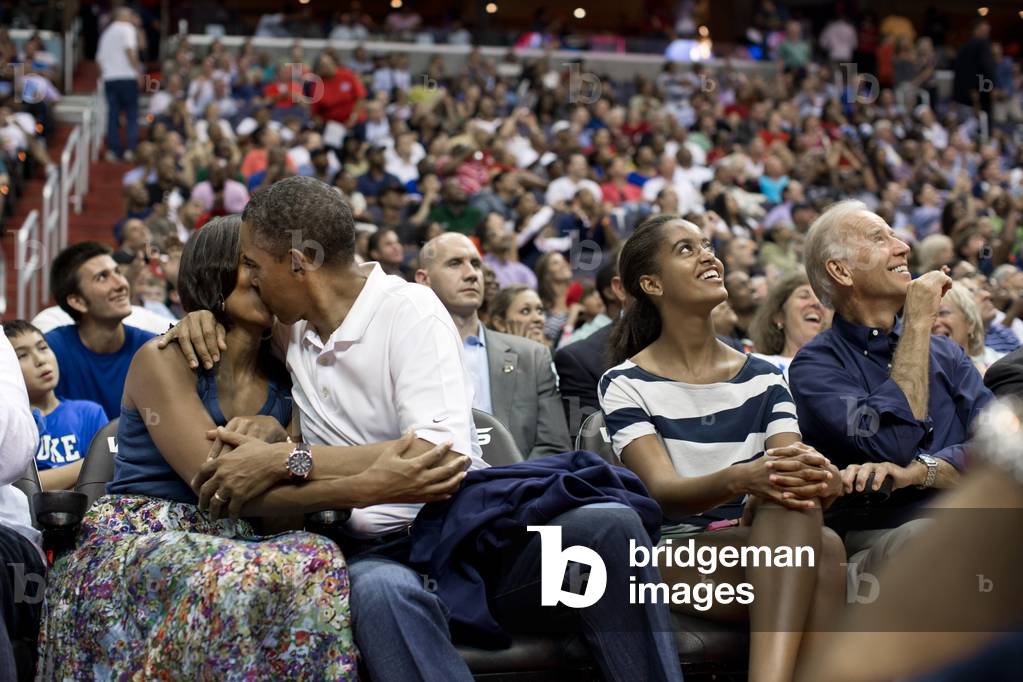 President Barack Obama kisses First Lady Michelle Obama for the 'Kiss Cam'. Malia and Joe Biden watch the kiss on Jumbotron screens the Verizon Center in Washington, D.C. July 16, 2012. They were attending the U.S. Men's Olympic basketball team's game against Brazil