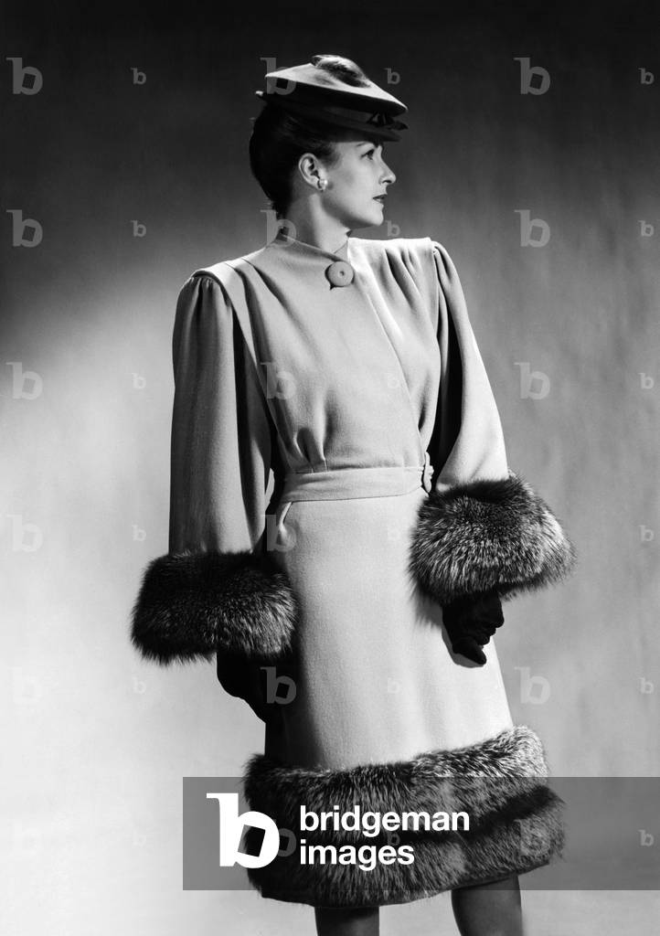 Luxurious fur trimmed dress of 1945, by Hans Geiger of New York. It features extremely broad padded shoulders, with bodice fullness shaped by pleats at from the shoulder seams. The front closure is accented by one large button at the neck
