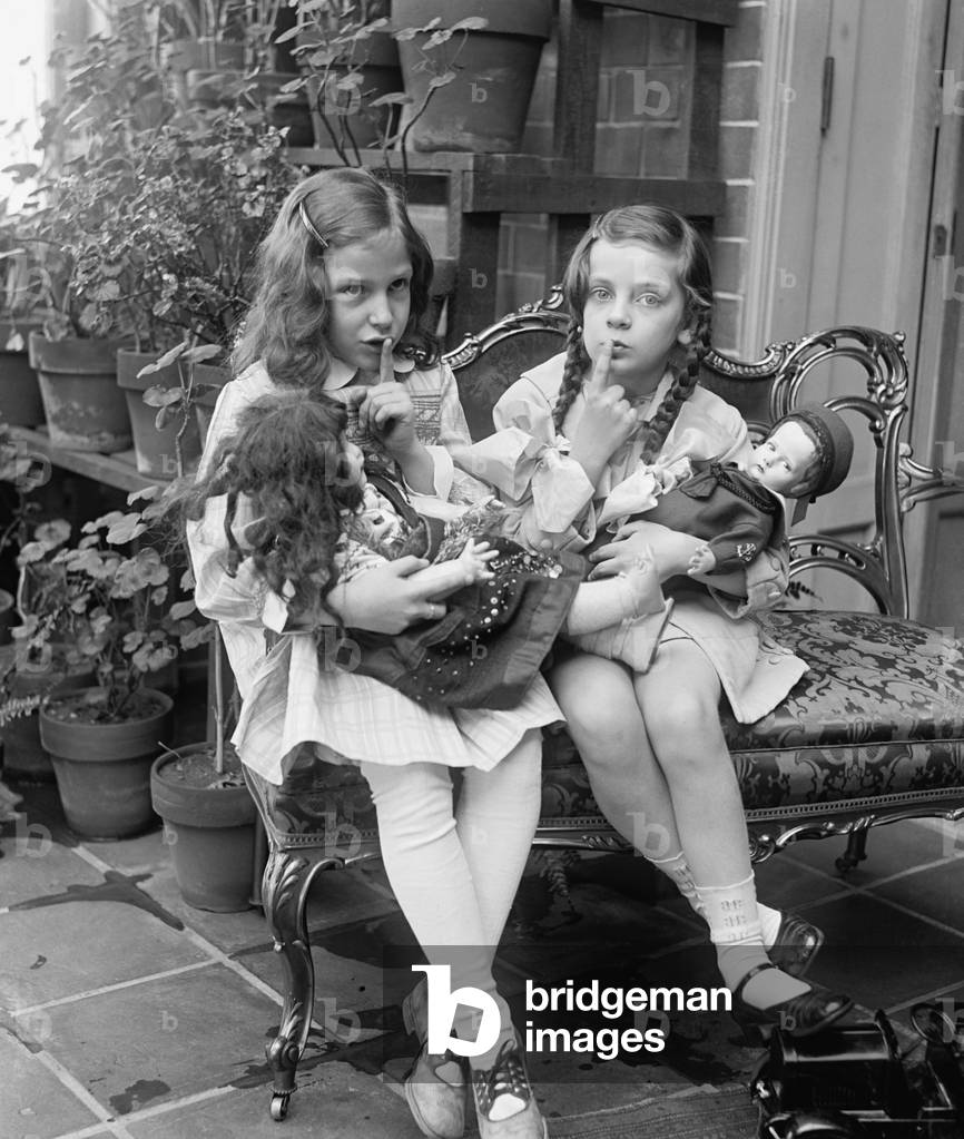 Two young girls with dolls, c. 1920. They ask for quiet as they pretend their dolls are asleep