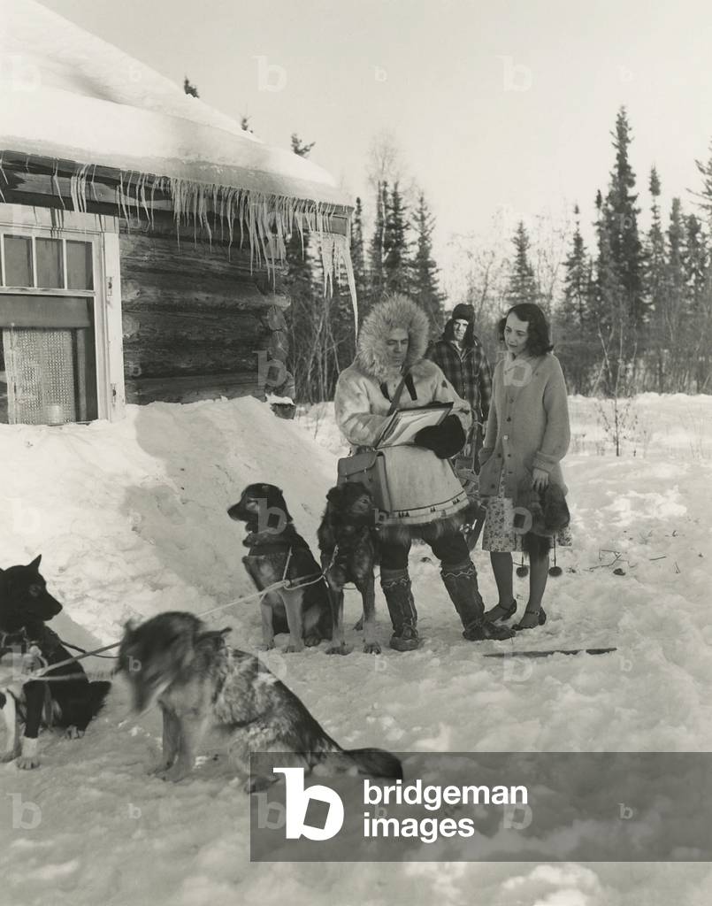 1940s Census taker in Fairbanks, Alaska. He traveled by dog sled to reach this woman's home. The dog musher stands in the background, so he does not overhear the confidential census information