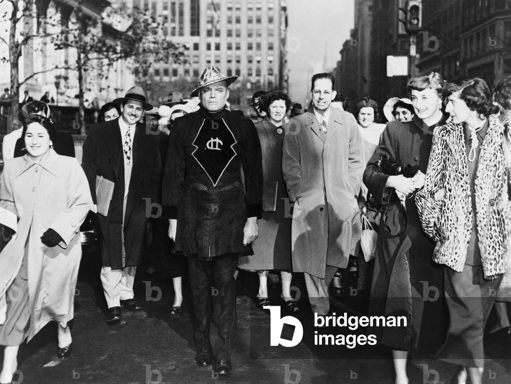 A laughing crowd accompany a man dressed in a 'Martian' costume crossing a street in Mid-town Manhattan on November 6, 1950