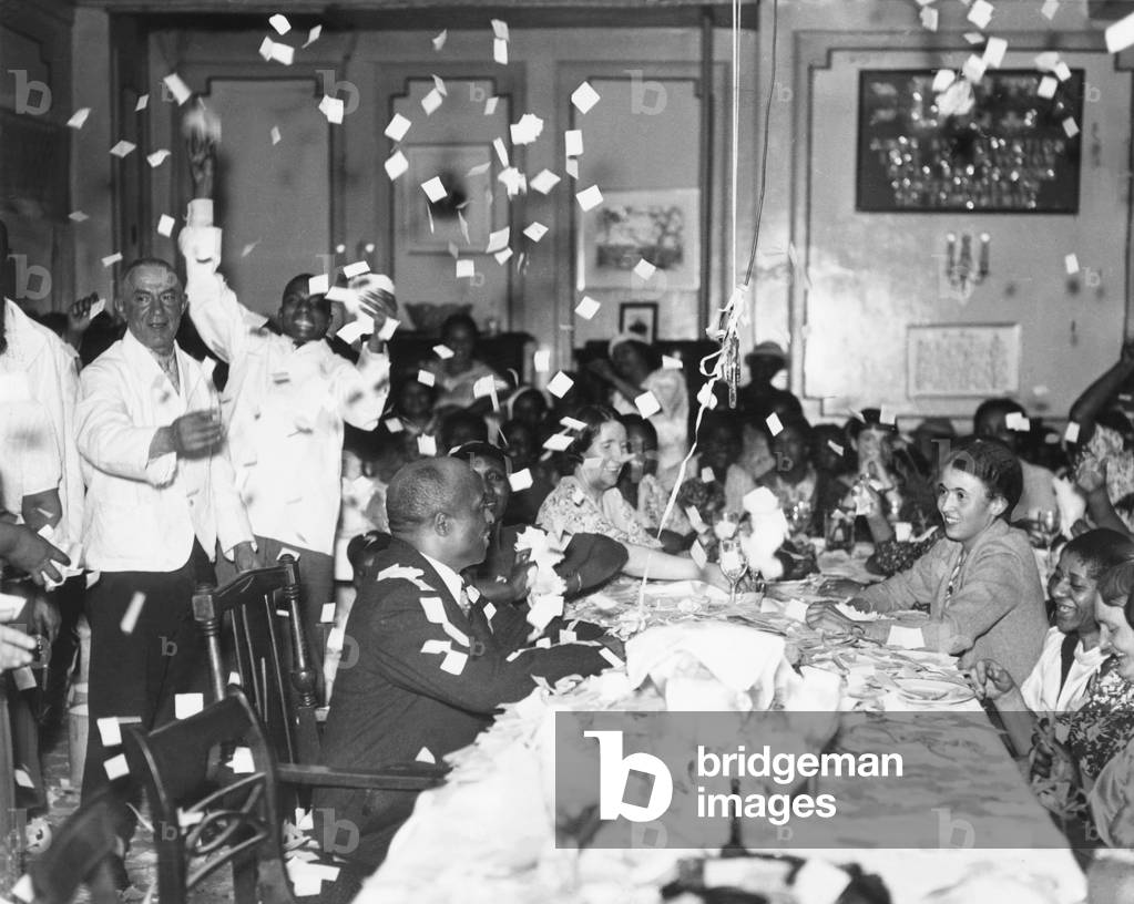 Jubilant scene in Father Divine's Harlem 'Heaven No. 1'. Father Divine beams on them from his accustomed place at the head of the table. The celebration immediately followed the African American evangelist's release on $ 500 bail on a felonious assault charge. April 23, 1936. -
