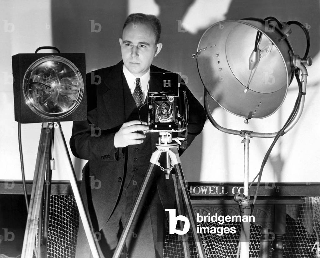Dr. Harold Edgarton, of M.I.T., stands behind his camera that boasts ultra-speed photography, with pictures being taken at 1/100,000th of a second. 12/7/38.