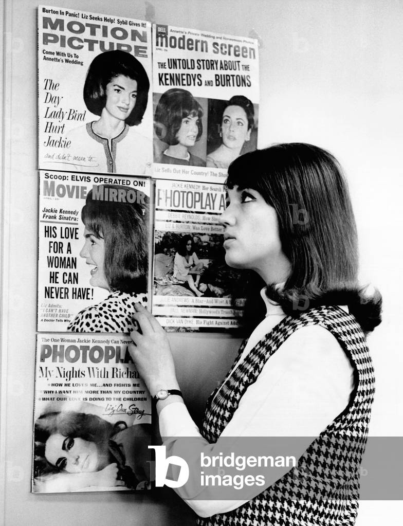 A young women observes a display of celebrity gossip magazine covers featuring widowed First Lady Jacqueline Kennedy and the often married actress Elizabeth Taylor. Mar. 28, 1965