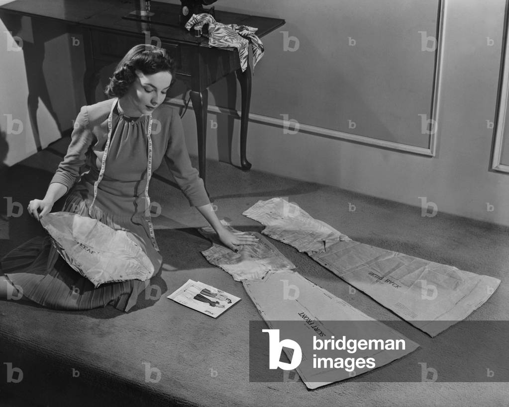 In the 1940s, many women continued to sew their own clothing. Fashionable patterns were distributed nationwide. In the background is a contemporary Singer Sewing machine. 1943