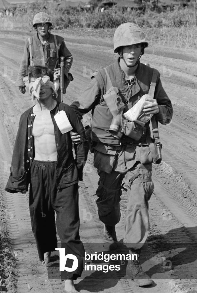 Vietnam War. A Viet Cong prisoner captured during Operation Double Eagle, 20 miles south of Quang Ngai, Vietnam is brought into the collection area by Marines. Prisoners are blindfolded and tied to prevent escape attempts. The card on the prisoner's black pajama shirt relates to circumstances of his capture