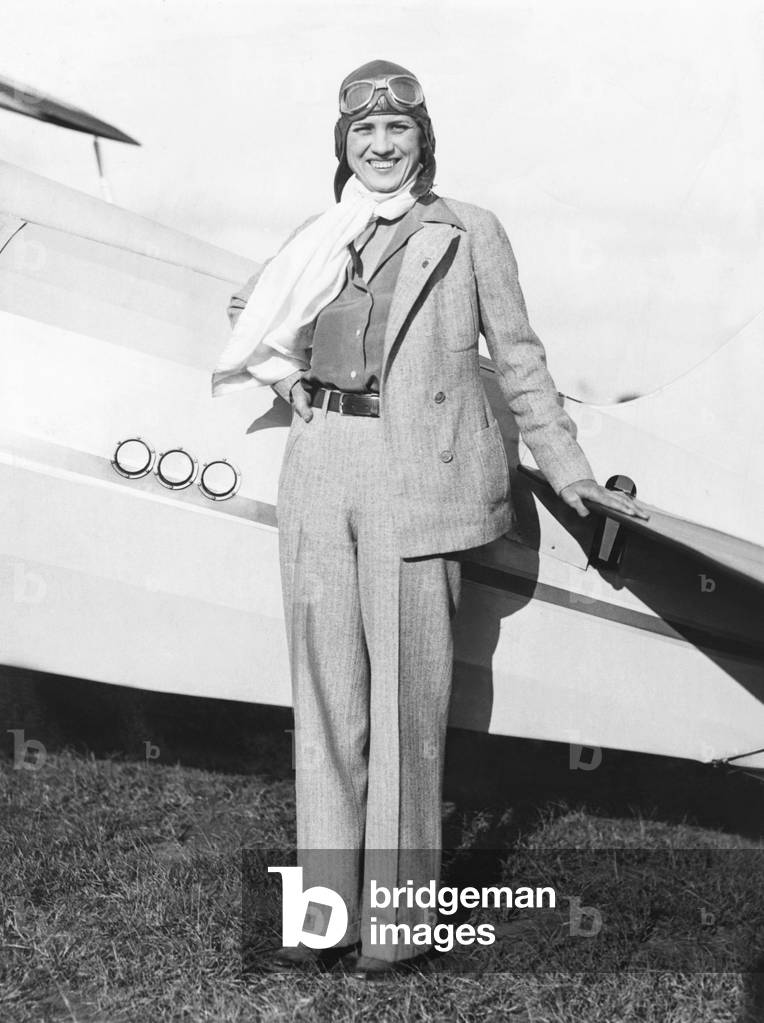 Jacqueline Cochran, sports woman pilot, at Roosevelt Field NY with her monoplane. Jackie Cochran is now preparing for the forthcoming National Air Pageant. She wears a trouser suit of imported gray tweed, soft sport shirt, and scarf of white parachute silk. Oct. 5, 1933 -
