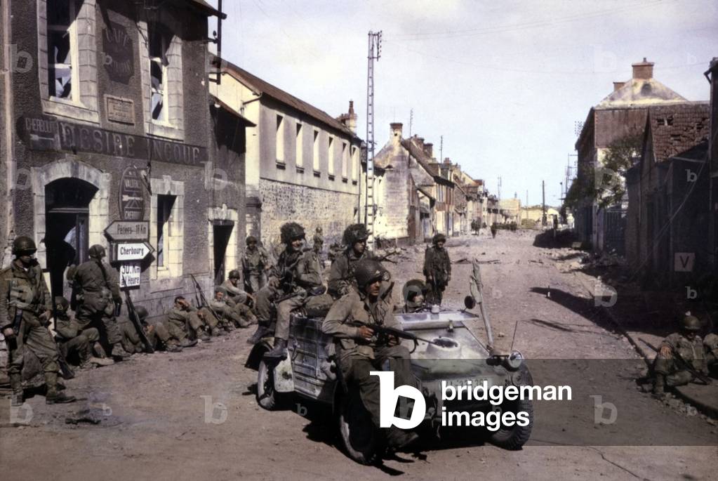Bataille de Carentan: U.S. Airborne troops patrolling the streets of Carentan in a captured German Volkswagen. June 12-18, 1944. Carentan was one of the first objectives captured after the D-Day. Normandy Campaign, France, World War 2. B&W Photo with oil color. (JTHIS_2014_3_103)
