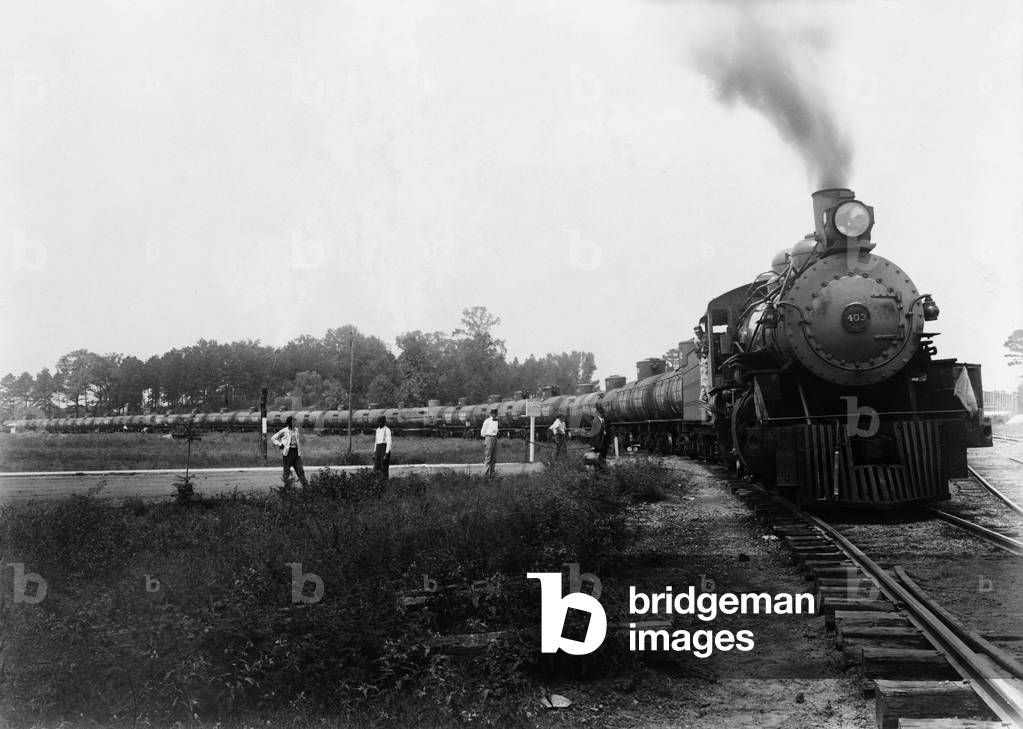 Pedestrians waiting at a railroad crossing for Louisiana Arkansas Railroad train pulling tank cars to pass. c. 1920-1940. LC-USZ62-106094