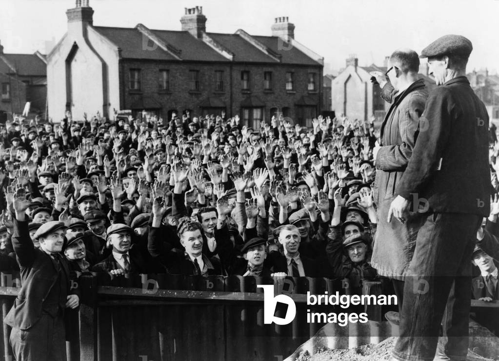 Strikers at the Royal Albert Docks, London, raising their hands in a vote of confidence for strike leader Thomas Powell, seen in right foreground, wearing glasses. 1945