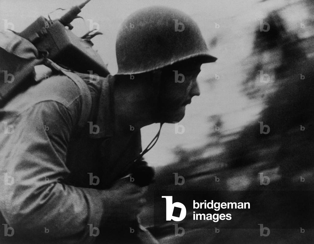 A Marine runs across the beach on Peleliu Island, Sept. 1944. He is a World War 2 'radio man', with a walkie talkie strapped to his back and a radio phone in his right hand. World War 2, Pacific Ocean