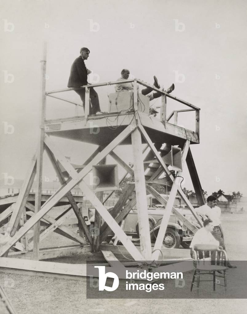 Knute Rockne, seated on coaching tower, as he overlooks the football field at South Bend. Rockne directs the action through the advanced technology of loud speakers. Sept 17, 1930.