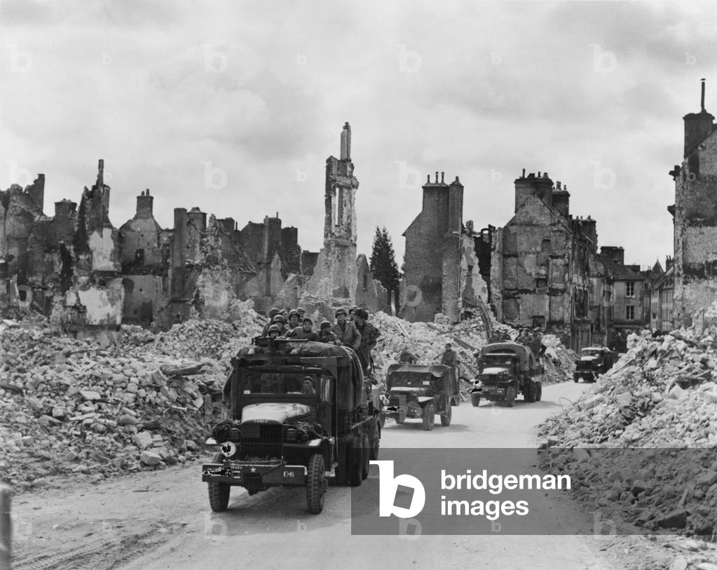 Trucks, some with U.S. soldiers standing in back, riding through the ruins Valognes, France. June-July 1944. Normandy Campaign, World War 2