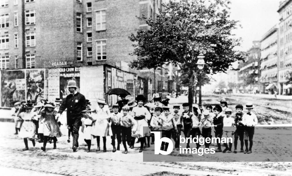 Policeman helping a group of neighborhood children cross the street in N.Y.C. in 1910.