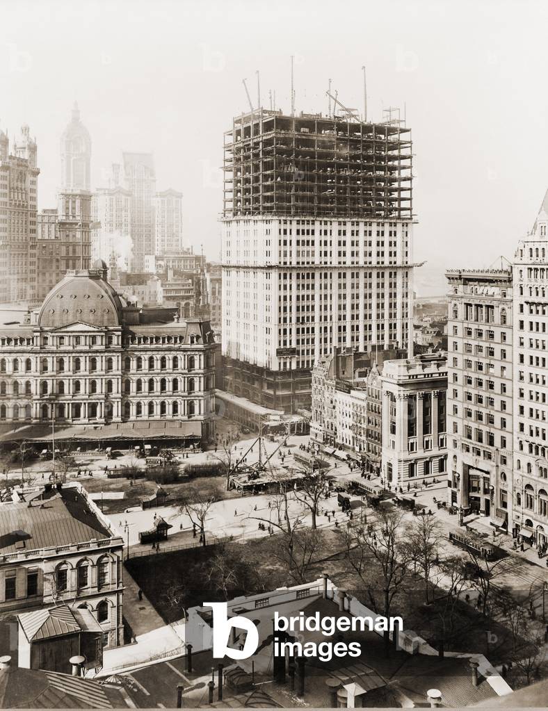 Woolworth Building, partially-constructed building amidst smaller buildings. The lower floors have received a white terra-cotta facing worked in lacy Gothic style. Photo made April 4th, 1912