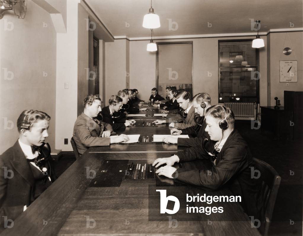 High technology in 1928 was the NY Stock Exchange's new quotation system. Photo shows men with headphones and mouthpieces working in the new quotation room