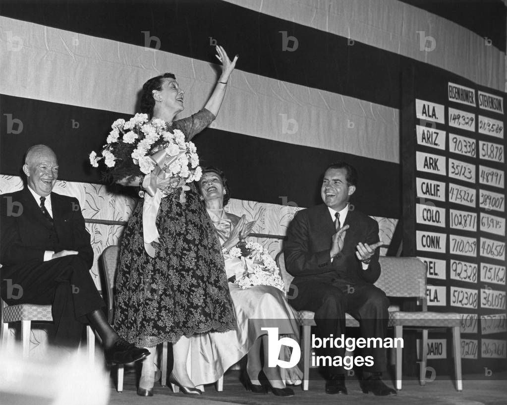 Mamie Eisenhower waves to the Republican crowd at the election night Victory Party. President Eisenhower is seated with Pat and Richard Nixon.
