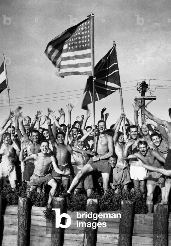 Thin Allied prisoners of war at Aomori Camp near Yokohama, Japan, cheer their rescuers. They are waving flags of the United States, Great Britain, and Holland. August 29, 1945 at the end of World War 2