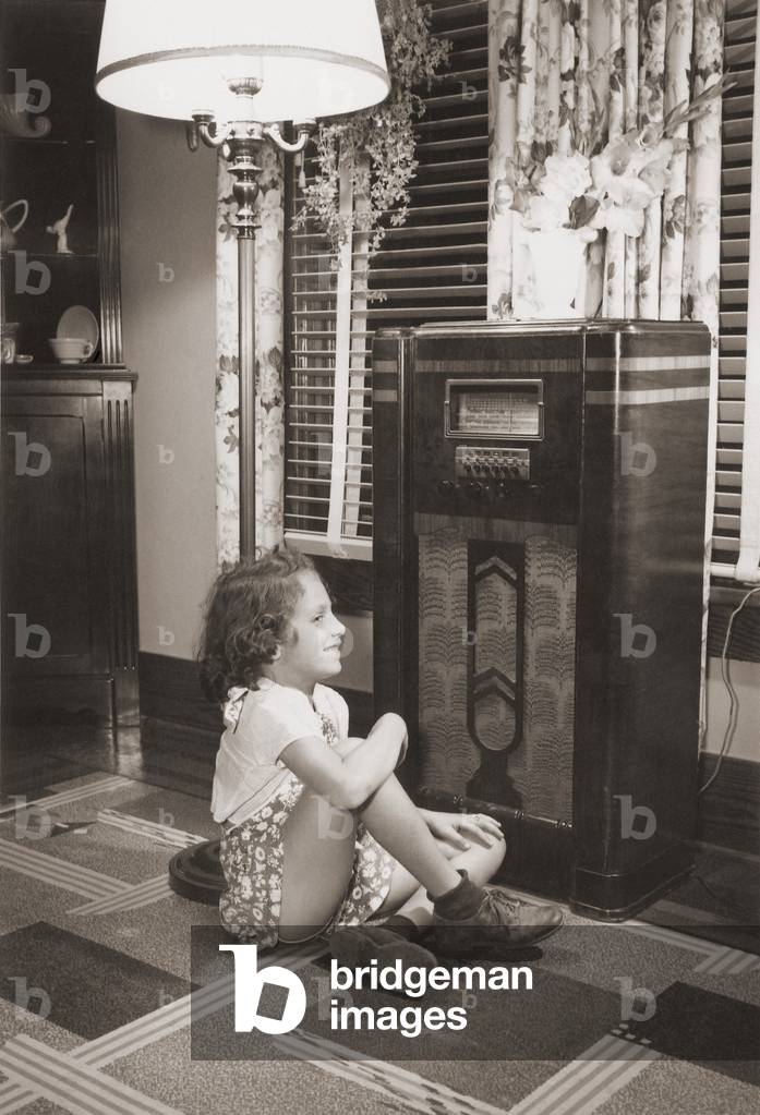 Little girl smiles as she enjoys a radio program in the 1930s