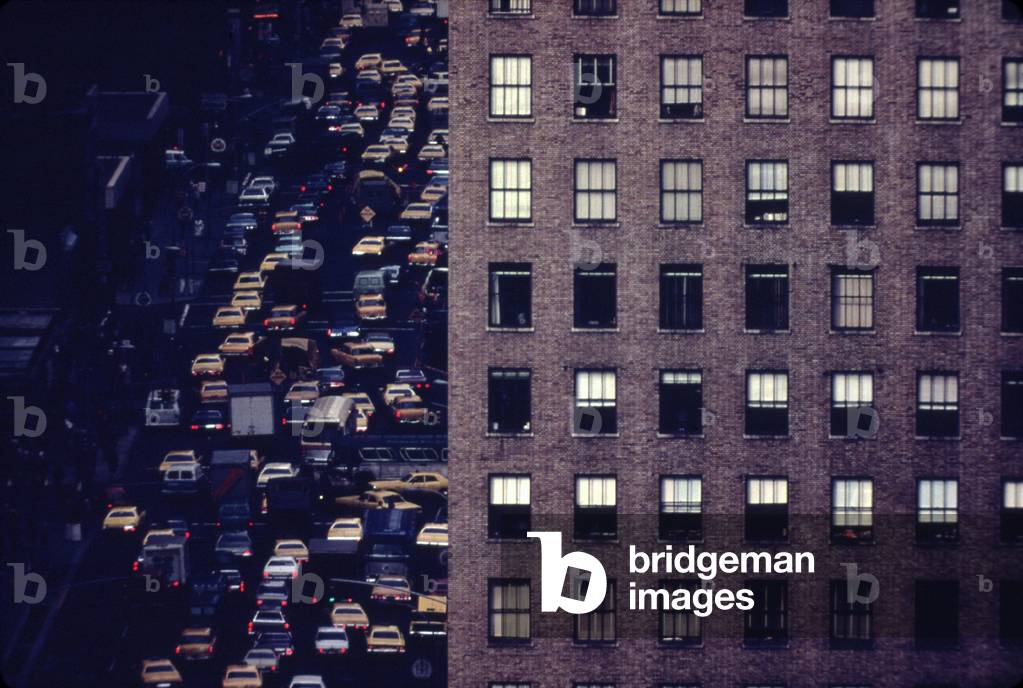 Traffic in New York City. View of vehicles on Manhattan's Sixth Avenue at 42nd Street is framed by a massive pre-war apartment building. c. 1973-75