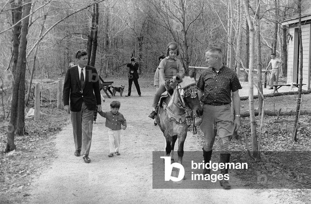 Kennedy family weekend at Camp David. President Kennedy, walks with his 2 year old son John Jr., and Caroline Kennedy rides a pony named Tex. The pony was a gift from Vice President, Lyndon Johnson. March 31, 1963