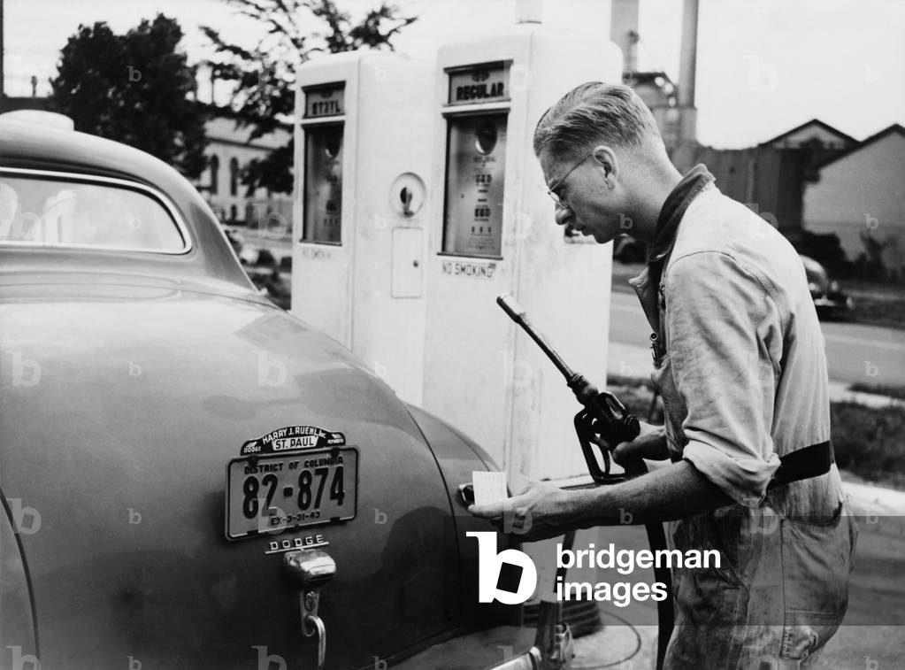 An automobile service station attendant measures out gasoline in accordance with the World War II gasoline rationing. July 1942